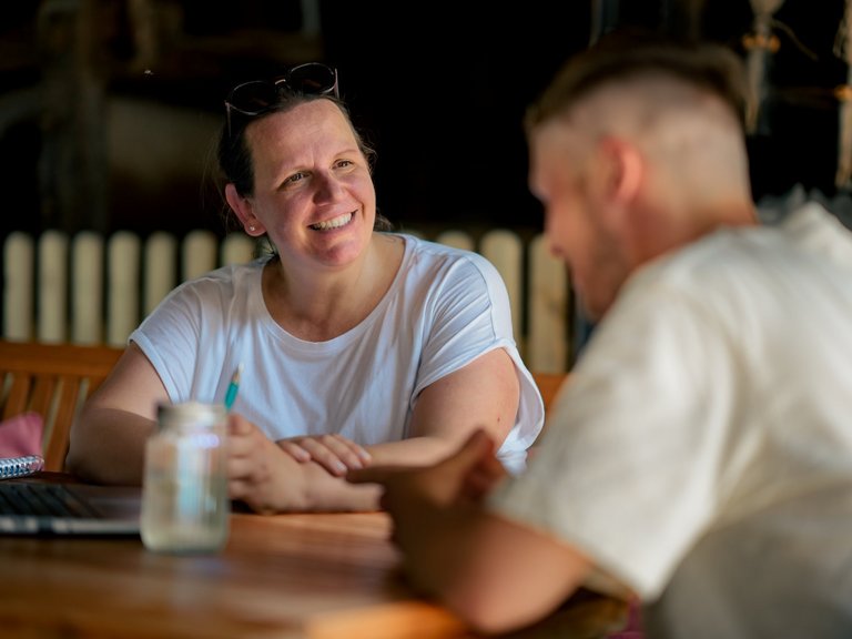 Eine Frau und ein Mann sitzen an einem Tisch und unterhalten sich lächelnd.