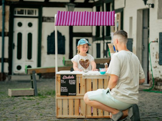 Ein junges Mädchen verkauft einem Papa an einer Spieleeisdiele ein Eis.