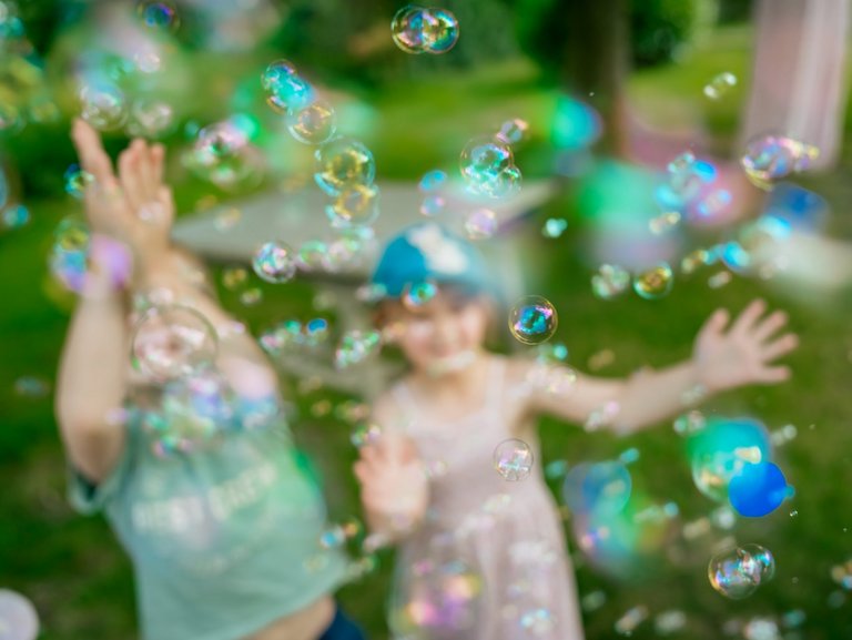 Zwei Mädchen versuchen auf einer Wiese Seifenblasen zu fangen.